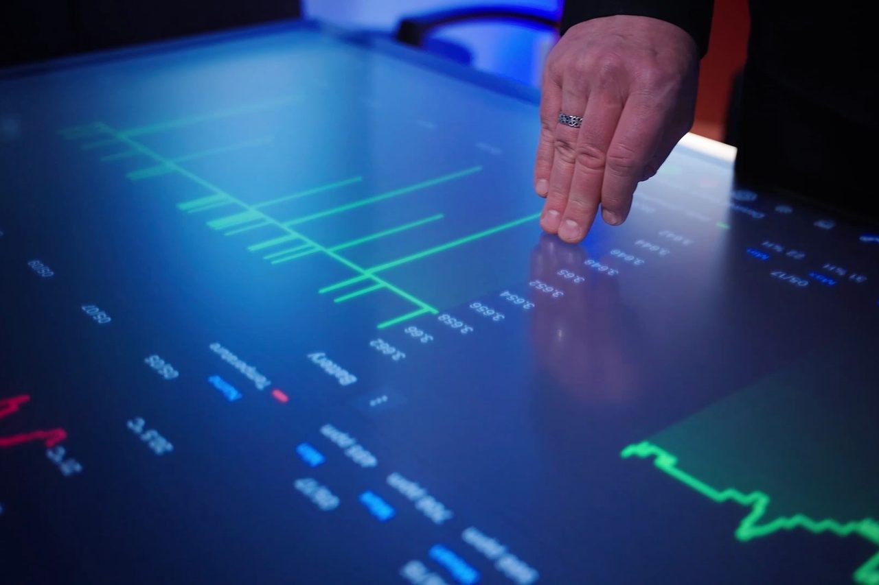 A hand on a touchscreen UI table, with measurement graphs shown on the surface.