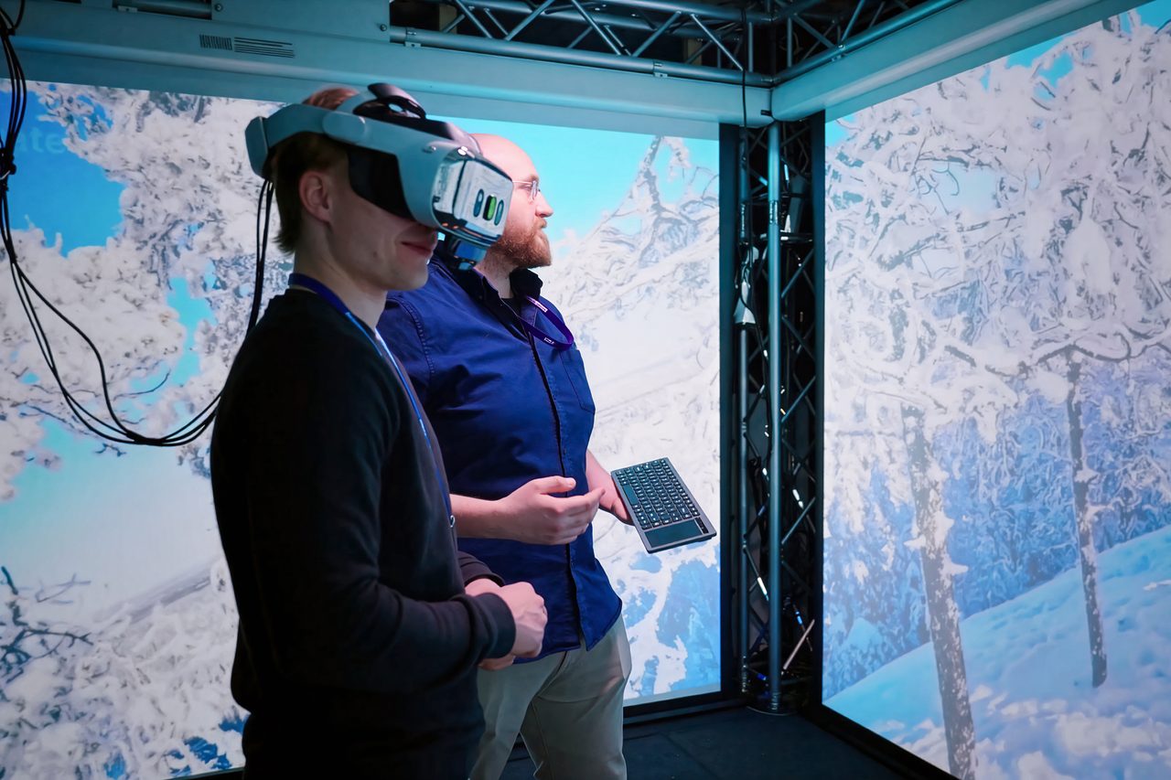 Two people in the Immersion Zone, one wearing a virtual reality headset, with a snow-covered landscape projected on the surrounding walls.
